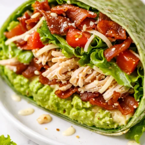 Fresh California club wrap cut in half revealing crisp bacon, avocado, and turkey layers on a golden tortilla.