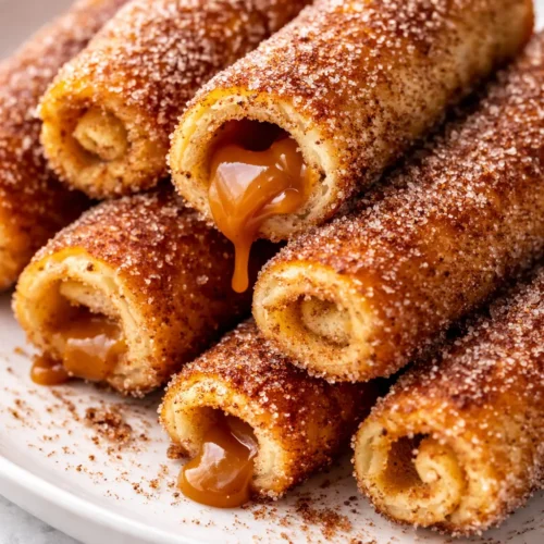Golden brown cinnamon sugar french toast roll-ups filled with creamy spread, dusted with powdered sugar, and drizzled with maple syrup on a plate.