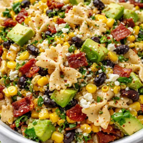 Creamy corn pasta salad with crispy bacon, diced avocado, and tangy dressing in a serving bowl