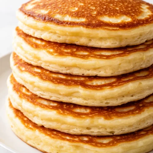 Stack of fluffy golden-brown pancakes with melted butter and maple syrup, garnished with fresh blueberries.