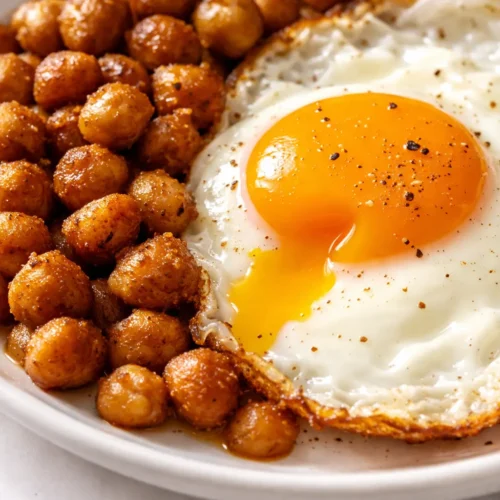 Spiced chickpea fried eggs with runny yolks and crispy edges on a bed of aromatic chickpeas, garnished with fresh herbs.