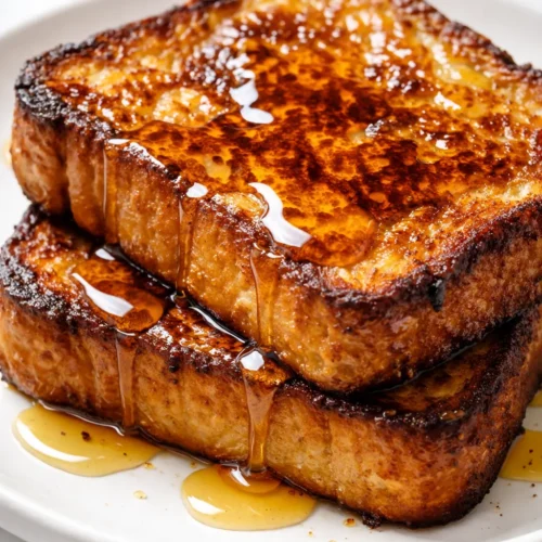 Golden vegan French toast slices with crispy edges, drizzled with maple syrup and topped with fresh berries, on a plate.