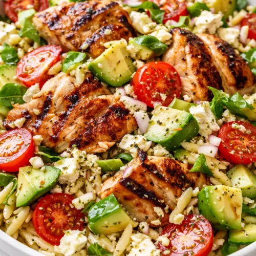 Bright lemony grilled chicken orzo salad with creamy avocado, featuring tender chicken, al dente orzo, fresh greens, and ripe avocado slices with lemon wedges.