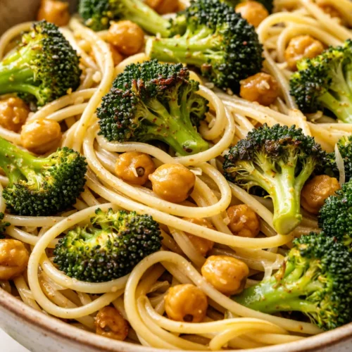 Steaming bowl of creamy broccoli chickpea pasta with al dente pasta, vibrant green broccoli florets, and tender chickpeas in a light sauce, topped with parmesan.