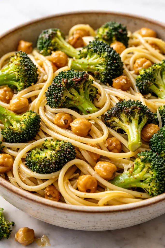 Steaming bowl of creamy broccoli chickpea pasta with al dente pasta, vibrant green broccoli florets, and tender chickpeas in a light sauce, topped with parmesan.