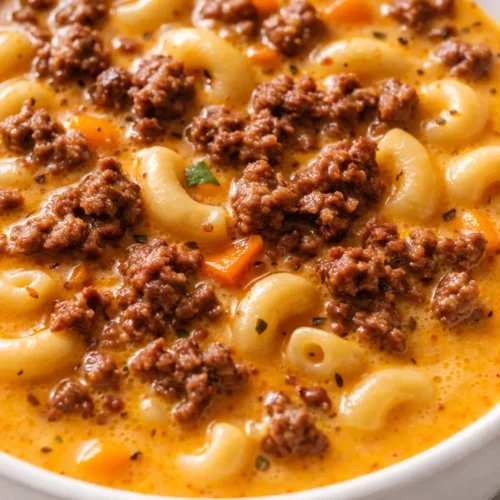 Bowl of creamy cheeseburger macaroni soup with ground beef, melted cheddar, and elbow macaroni, topped with fresh green onions and shredded cheese.