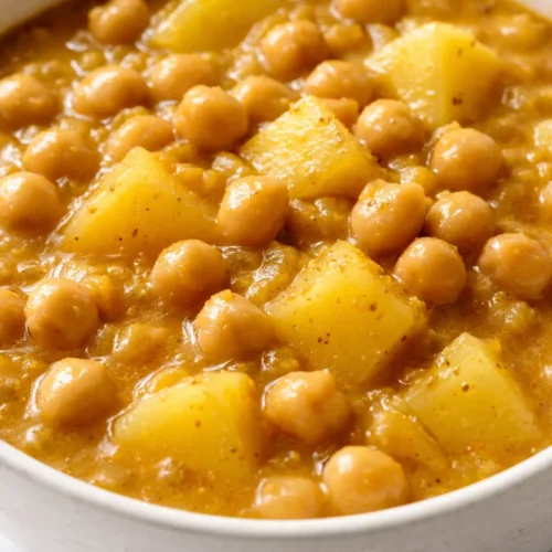 Bowl of chickpea potato curry with creamy golden sauce, tender potatoes, and chickpeas, garnished with fresh cilantro.