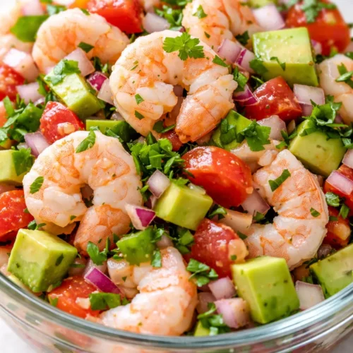 Citrus-cured shrimp ceviche in a glass bowl with vibrant diced tomatoes, onions, cilantro, and avocado slices, garnished with lime and tortilla chips.