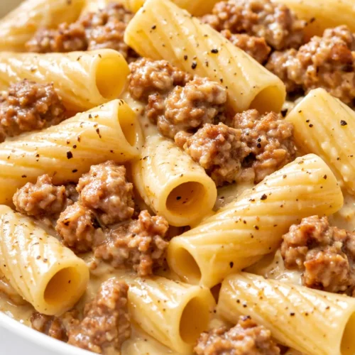 Rich creamy sauce coating rigatoni pasta with savory sausage pieces and fresh spinach leaves.