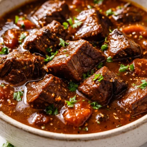 Deep smoky beef goulash in a bowl, thick red sauce with tender beef chunks, sprinkled with fresh parsley, steam rising.