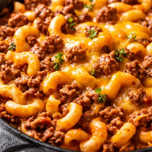Creamy, cheesy taco mac with seasoned ground beef, melted cheddar, and fresh tomato and lettuce toppings in a bowl.