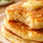 Fluffy Japanese soufflé pancakes stacked high, golden brown and dusted with powdered sugar, showing their tall airy texture