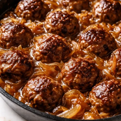 French onion meatball skillet with melted golden gruyere and caramelized onions over juicy meatballs in savory broth.