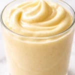 Creamy high protein banana pudding yogurt topped with sliced bananas and a sprinkle of cinnamon, thick and luscious texture.