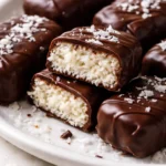 Dark chocolate coated homemade bounty bars with white coconut filling, cut to show layers, on a rustic wooden board