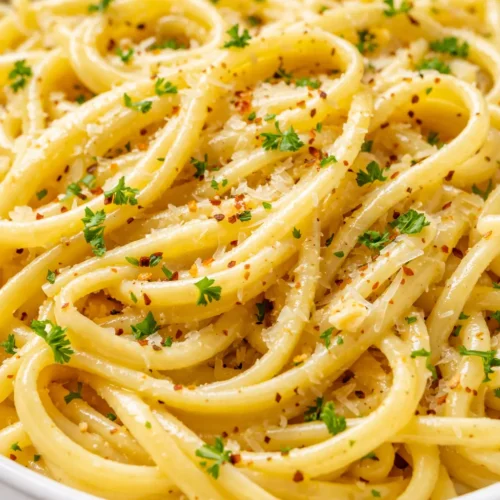 Lemon butter garlic pasta sauce coating spaghetti, creamy silky texture, bright yellow hue from lemon, golden garlic bits, garnished with parsley.