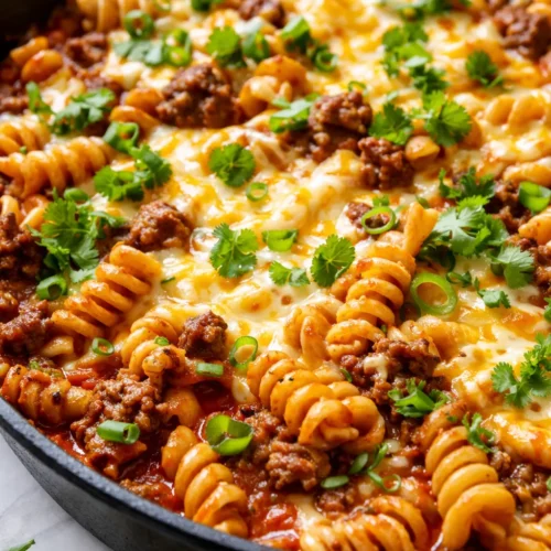 Creamy one-pan enchilada pasta with melted cheese, sour cream, and black beans, garnished with cilantro and diced tomatoes on a dark plate.
