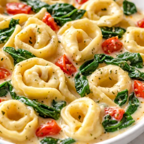 Creamy one pot spinach tomato tortellini in a white bowl with visible swirls of cream and flecks of green spinach and red tomatoes, garnished with fresh basil.