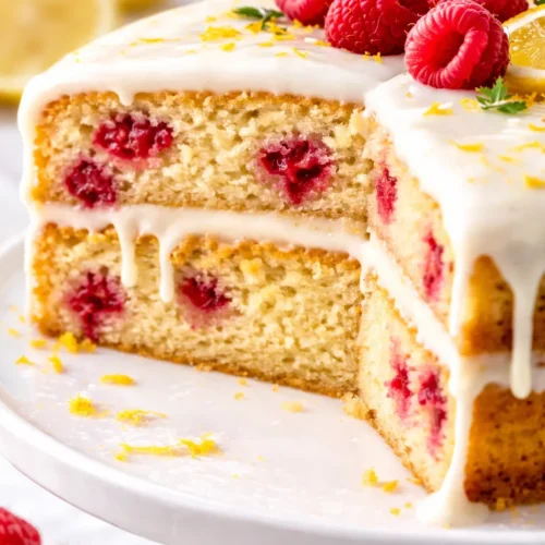Moist raspberry lemon cake layers with white chocolate frosting, topped with fresh raspberries and lemon zest.