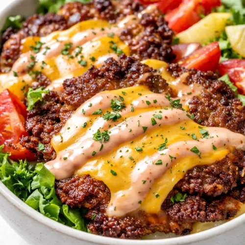 Smash burger bowl with crispy crust patties, melted cheddar, fresh lettuce, and tomato over fries, drizzled with special sauce.