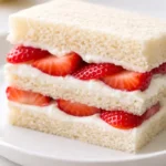 Fluffy strawberry cream tea party sandwiches on a platter with fresh strawberries and mint, delicate pink filling.