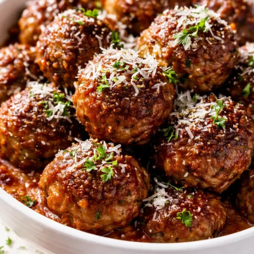Rich, herby Sunday gravy meatballs in a deep red tomato sauce, garnished with fresh basil and parsley, golden brown and tender.