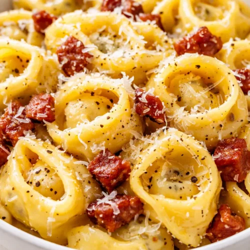 Rich and creamy tortellini carbonara with crispy pancetta and Parmesan, served in a white bowl with a fork