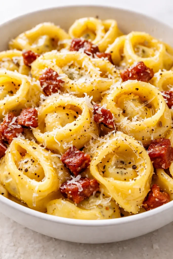 Rich and creamy tortellini carbonara with crispy pancetta and Parmesan, served in a white bowl with a fork