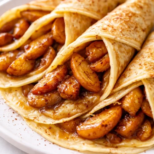 Stack of tender apple cinnamon crepes drizzled with caramel sauce and dusted with cinnamon, golden brown and soft.