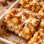 Golden apple pie Rice Krispie treats topped with whipped cream, cinnamon, and caramel drizzle on a rustic plate