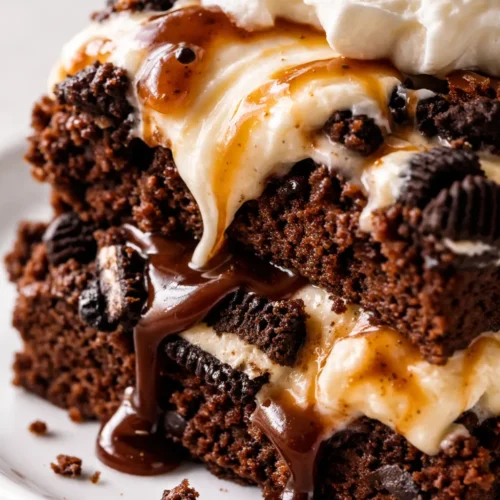 Tall slice of no-bake brownie ice cream cake with layers of fudgy brownie, vanilla and chocolate ice cream, Oreo pieces, and glossy hot fudge drizzle
