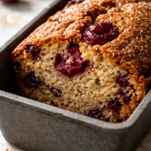 Moist Cherry Garcia loaf cake with cherry pieces and chocolate chips, golden crust, sliced on a wooden board
