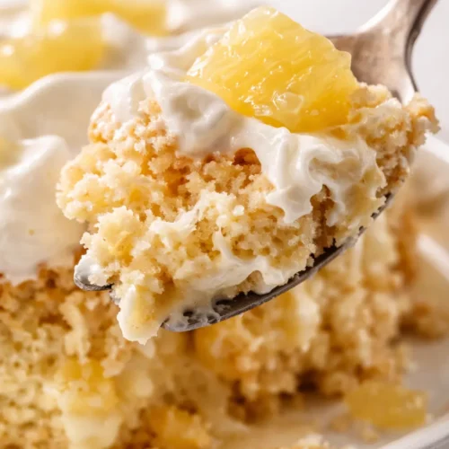 Fluffy pineapple tres leches cake on a white platter, topped with whipped cream and pineapple tidbits, showing an airy crumb and creamy soak