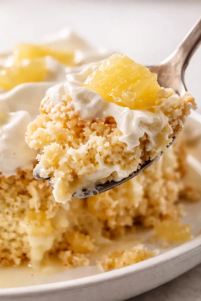 Fluffy pineapple tres leches cake on a white platter, topped with whipped cream and pineapple tidbits, showing an airy crumb and creamy soak