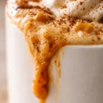 Steaming homemade pumpkin spice latte in a white mug with frothy milk foam and a sprinkle of pumpkin pie spice, on a rustic wood table