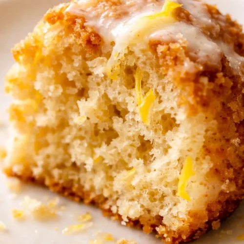 Tender lemon buttermilk cake with a golden brown crust and a dusting of powdered sugar on a white cake stand