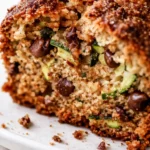 A slice of moist zucchini bread on a plate, showing its golden brown crust and tender crumb with visible flecks of green zucchini