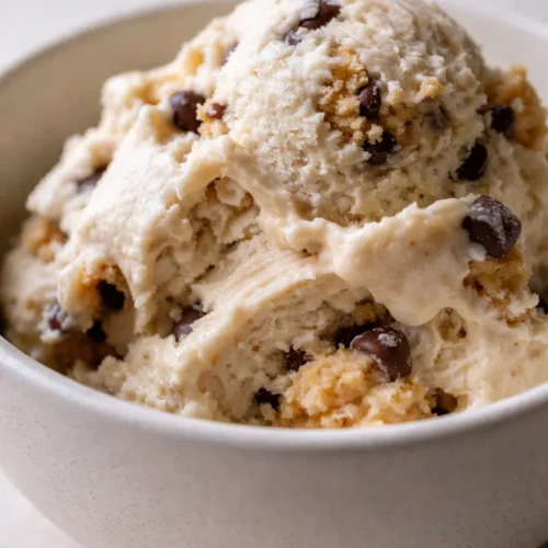 Creamy Ninja Creami cookie dough protein ice cream scoop with brown cookie dough chunks in a bowl, swirled vanilla base