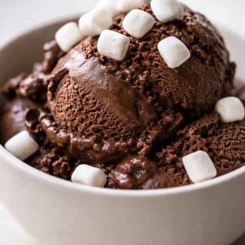 Smooth and creamy Ninja Creami frozen hot chocolate ice cream in a bowl with a rich chocolate color, topped with mini marshmallows