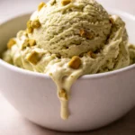 Creamy green pistachio ice cream topped with chopped nuts, showing smooth texture in a glass bowl