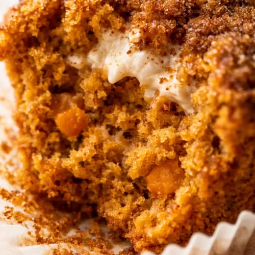 Pumpkin cupcake topped with creamy brown sugar cream cheese frosting, showing its moist crumb and warm fall colors