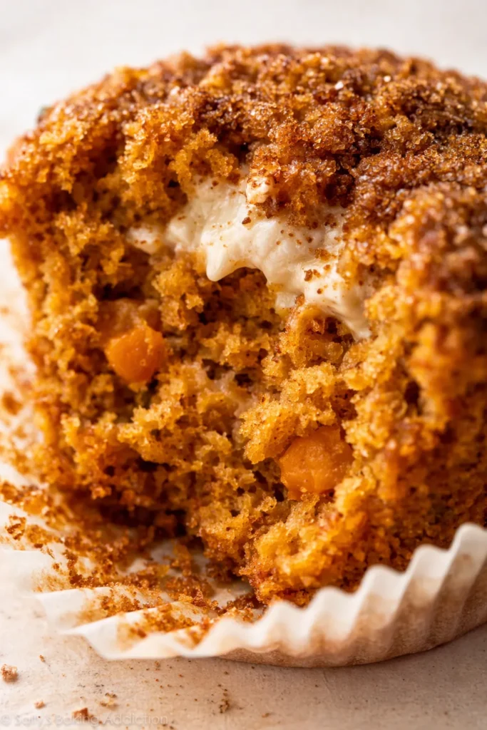 Pumpkin cupcake topped with creamy brown sugar cream cheese frosting, showing its moist crumb and warm fall colors