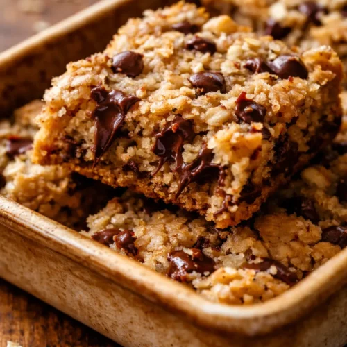 Golden brown oatmeal chocolate chip bars with melted chocolate chips, soft and chewy texture on a white plate