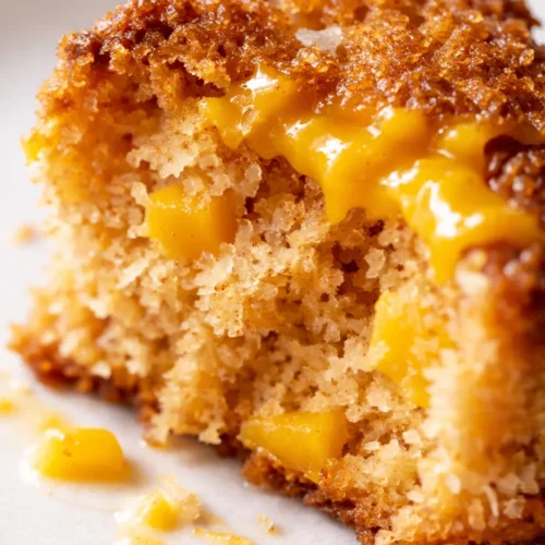 Moist vegan mango coconut cake slice on white plate, topped with fresh mango slices and shredded coconut, tropical and dairy-free