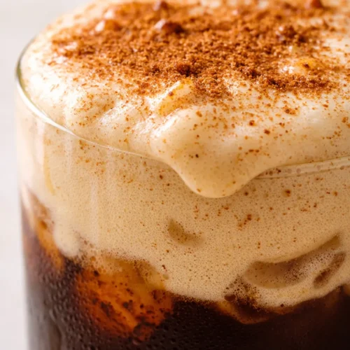 Tall glass of iced espresso topped with thick orange vegan pumpkin cream cold foam, creamy texture