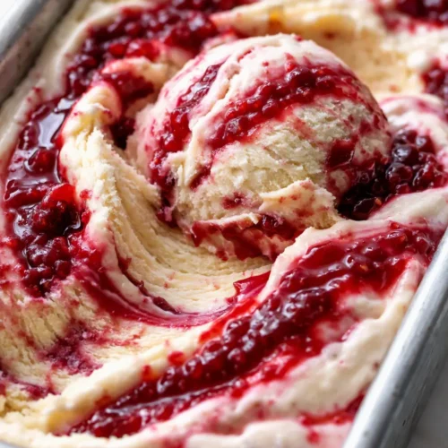 Creamy raspberry swirl ice cream with bright red ribbons against a pale pink base, smooth and velvety texture in a glass bowl.