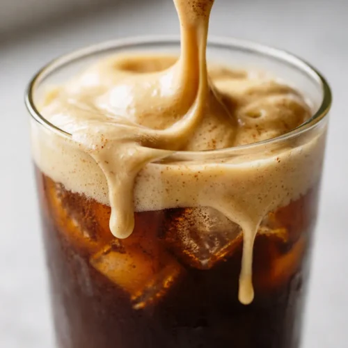 Iced chai latte with creamy pumpkin cold foam, layered milk and spiced tea, topped with airy orange foam