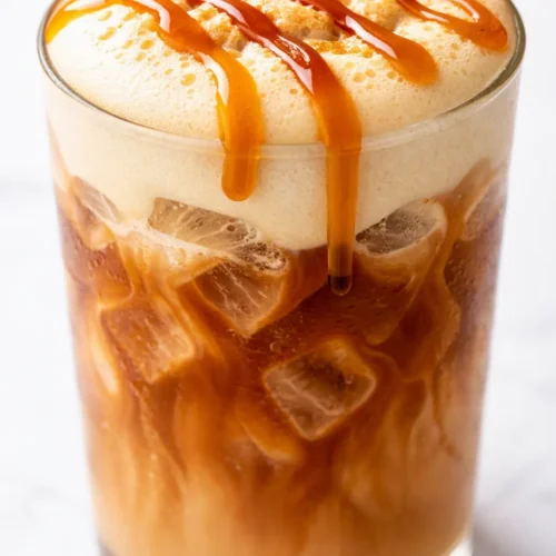 Iced pumpkin chai latte with almond milk, creamy orange-brown drink in a tall glass with ice and cinnamon on top.