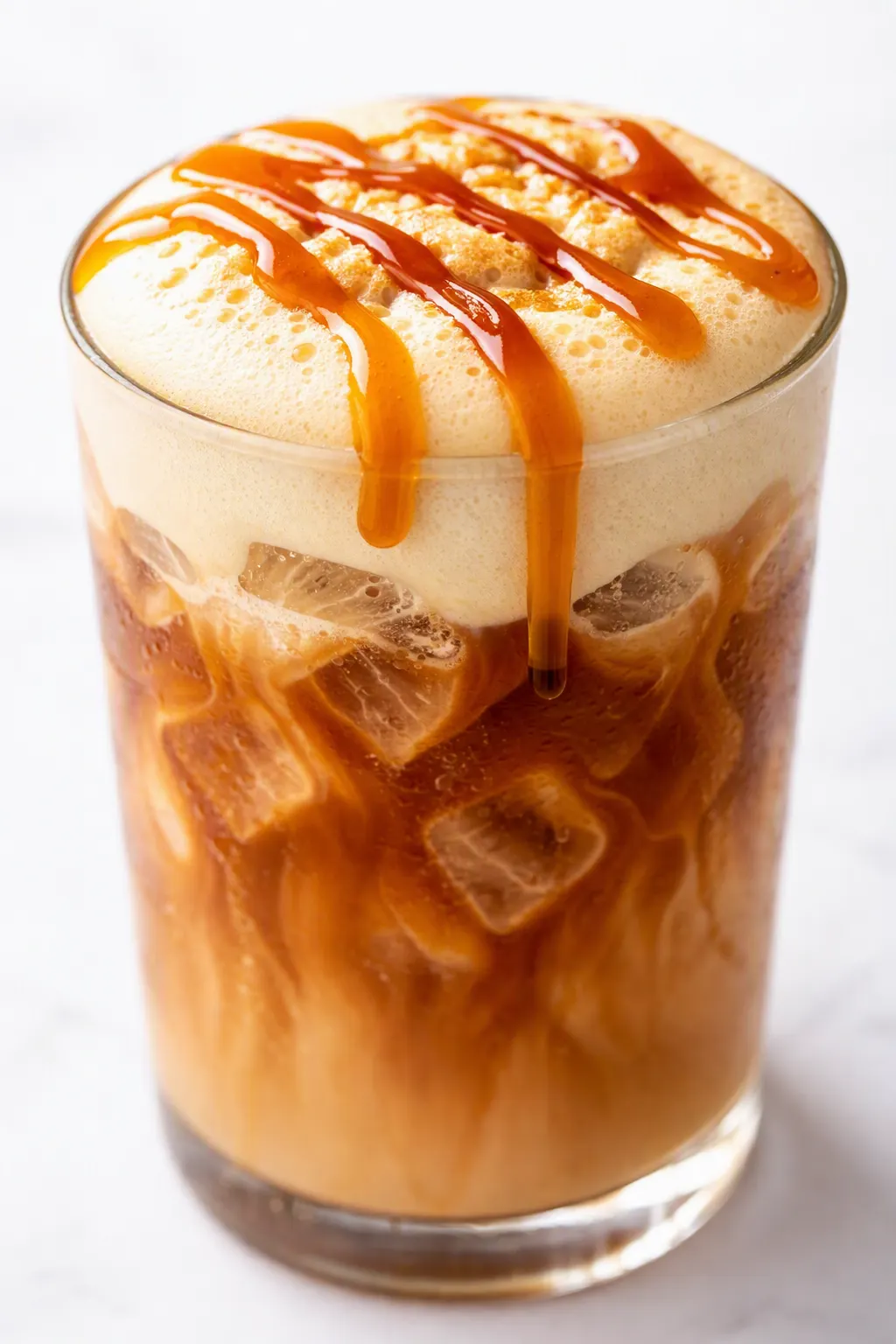 Iced pumpkin chai latte with almond milk, creamy orange-brown drink in a tall glass with ice and cinnamon on top.