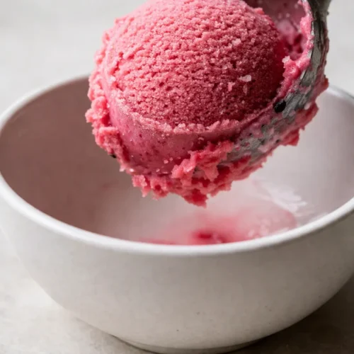 Raspberry sherbet from Ninja Creami with smooth creamy texture, vibrant pink color, and small raspberry pieces in a bowl